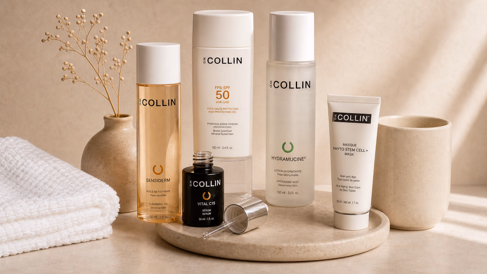 A row of G.M. Collin skincare, cleanser, SPF 50, serum and mask, arranged on a stone tray.