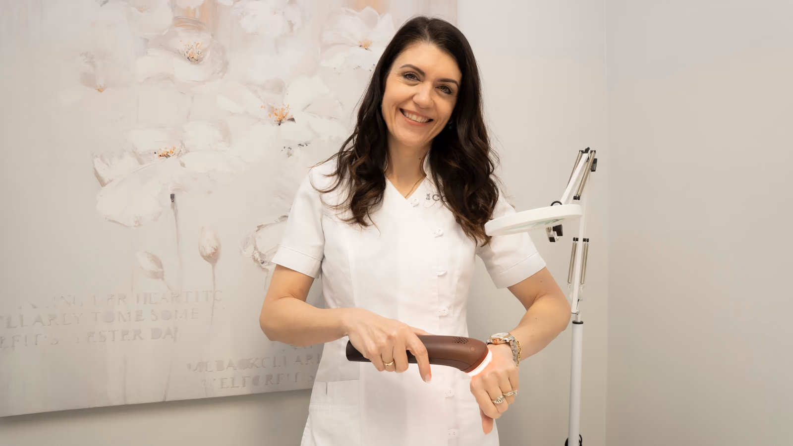 Krista McLean, co-owner of Sunwaves Facial Studio, smiling in the treatment room holding a facial device.
